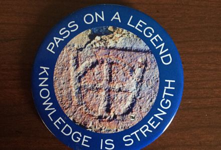 A round blue badge with a stone emblem and motivational text.