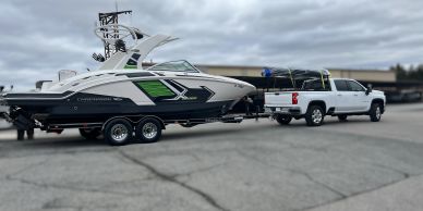 A white truck towing a black and white boat on a trailer under a cloudy sky.