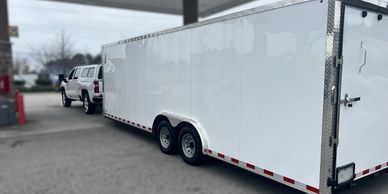 A white pickup truck towing a large white enclosed trailer.