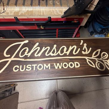 Wooden sign reading 'Johnson's Custom Wood' with decorative leaf design.