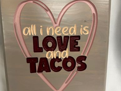 Sign saying 'all I need is LOVE and TACOS' inside a pink heart.