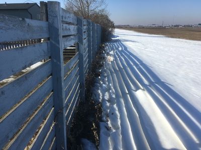 snow melting along lines of shadow from fence