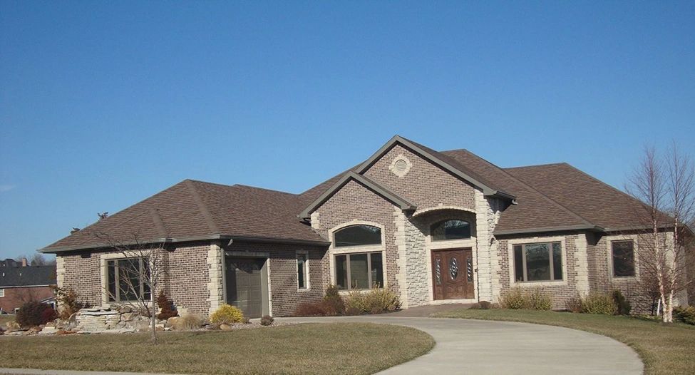 Modern brick house with a curved driveway and clear blue sky.