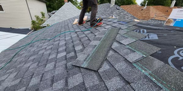 Worker installing gray asphalt shingles on a residential roof.