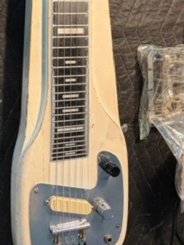 Vintage lap steel guitar placed on a padded surface with tools nearby.