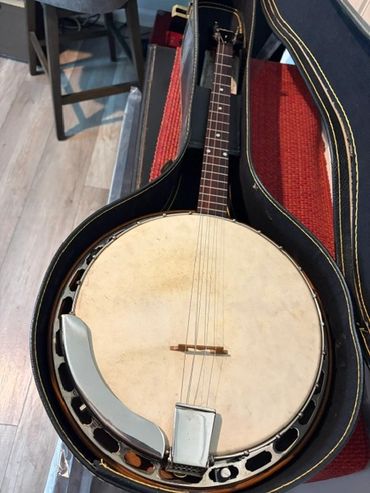 A vintage banjo resting in its open black case on a wooden floor.