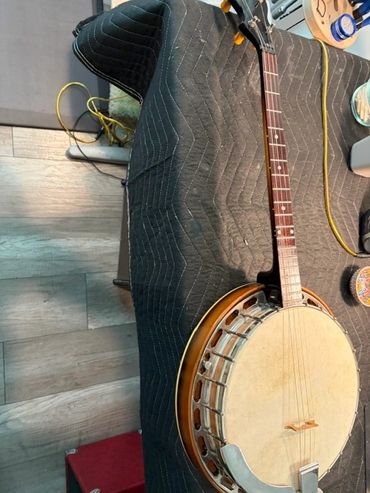 A banjo resting on a padded black blanket on a wooden floor.