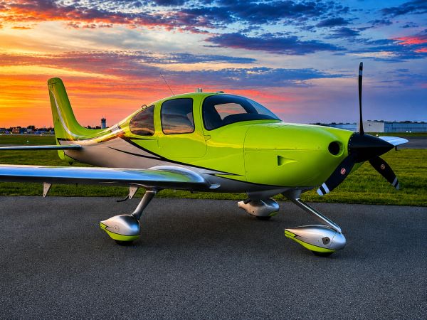Small green airplane on runway at sunset.