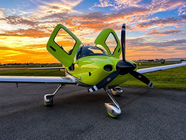 Bright green single-engine plane with doors open at sunset.