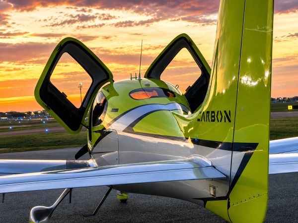 Small green and white plane with open doors at sunset.
