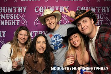 Five friends enjoying Country Music Night with drinks and cowboy hats.
