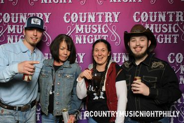 Four friends enjoying Country Music Night, dressed in casual country attire with drinks in hand.