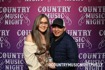 A smiling couple poses at a Country Music Night event with a purple backdrop.