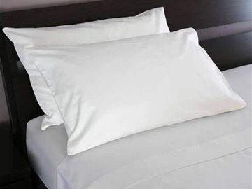 Two pillows lean against a black headboard on a bed.  All linens are white.