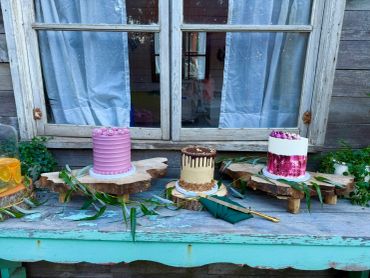 Three decorated cakes on wooden stands outdoors.