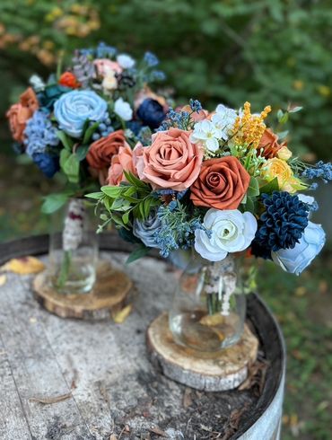 Two bouquets of colorful roses in glass jars on wooden rounds.
