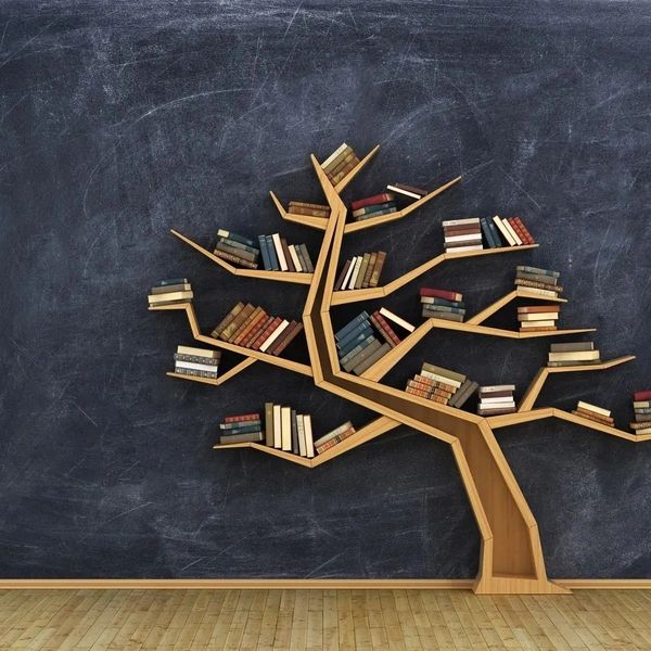 A tree-shaped wooden bookshelf filled with books against a dark wall.