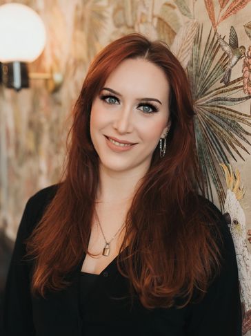 Smiling woman with long red hair standing by a decorative wall.