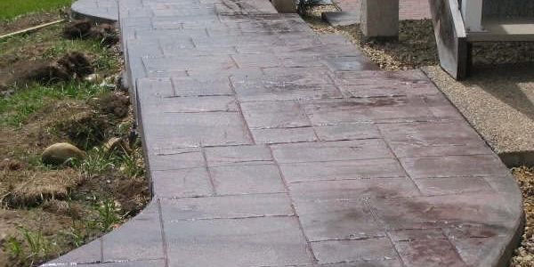 Stamped concrete walkway with a stone pattern next to grass and gravel.