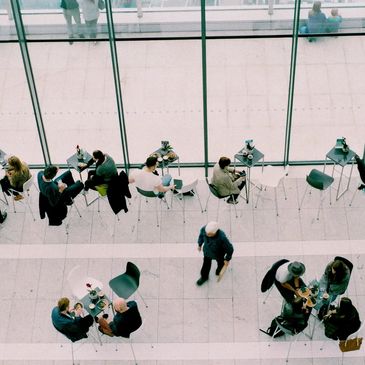 People sitting and walking in a modern café with large glass windows.