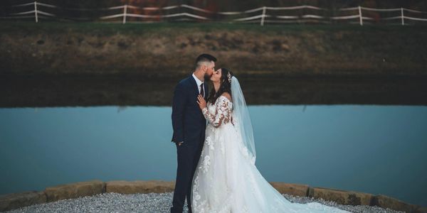 Bride and groom share a kiss by a peaceful lakeside at sunset.