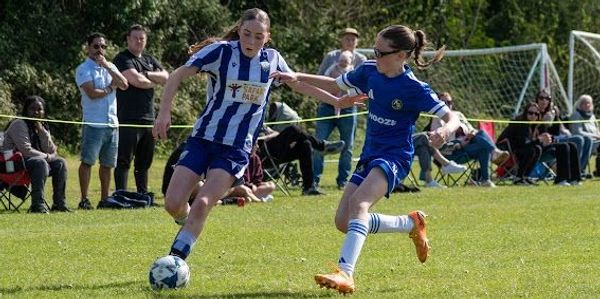 Two young girls compete intensely in a soccer match on a sunny day.