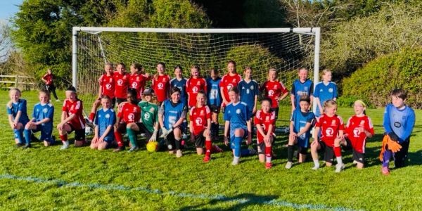 Two youth soccer teams posing together in front of a goalpost.