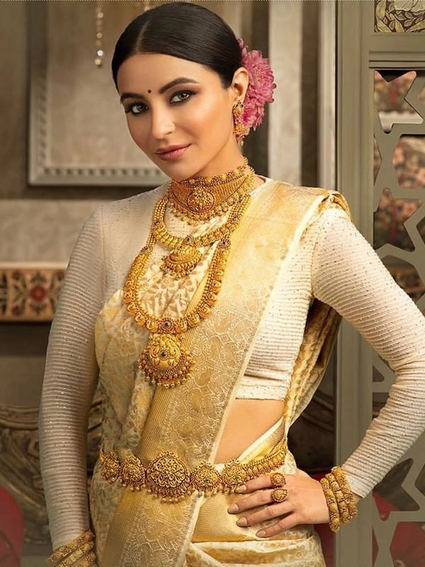 Woman dressed in elegant gold and cream traditional saree with intricate jewelry.