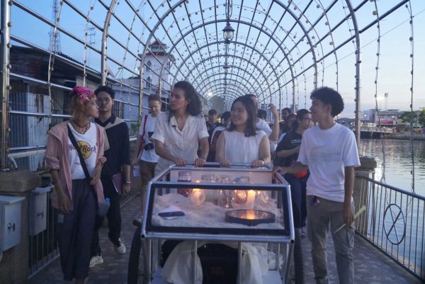Group of people walking under an arched light installation at dusk.