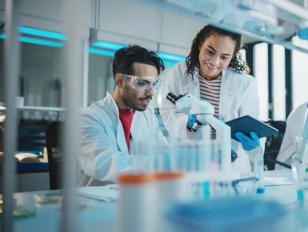 Scientists collaborate in a modern laboratory using a microscope and tablet.