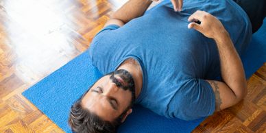 Man in blue shirt lying on yoga mat, appearing relaxed.