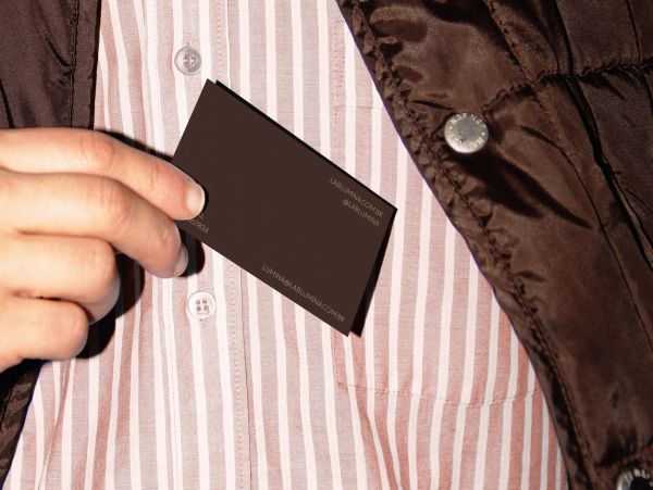 Hand holding a dark business card against a striped shirt and brown jacket.