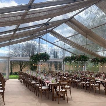 Elegant outdoor dining setup under a transparent canopy with hanging greenery and string lights.