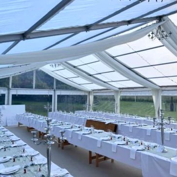 Elegant white tent set up with long tables and formal place settings for an event.