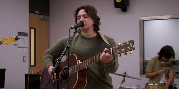 Young musician singing and playing guitar in a rehearsal room.