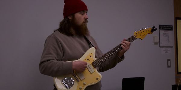 Man in a red beanie playing an electric guitar indoors.