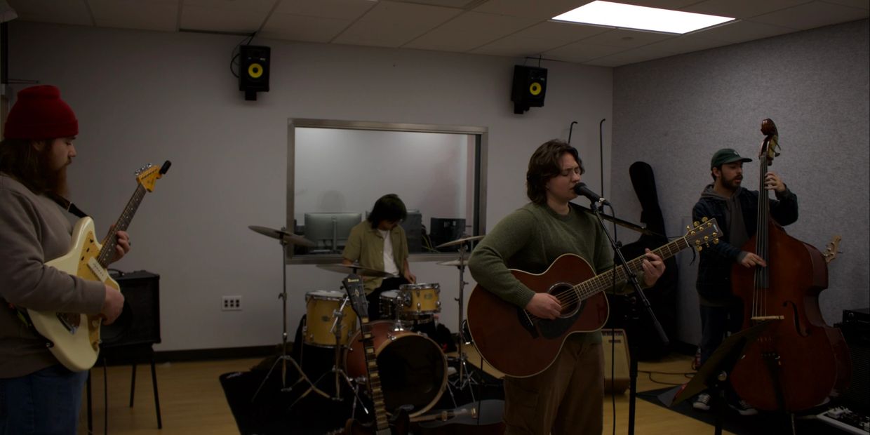 A band rehearses in a studio with guitars, drums, and a double bass.