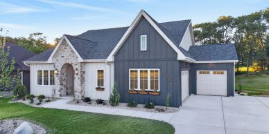Modern farmhouse with dark siding and stone accents under a clear sky.