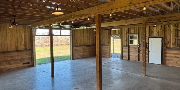Empty wooden barn interior with concrete floor and hanging lights.