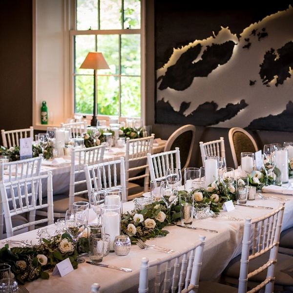 A metal image of the thousand islands behind a long white harvest table set with lush fresh garland.