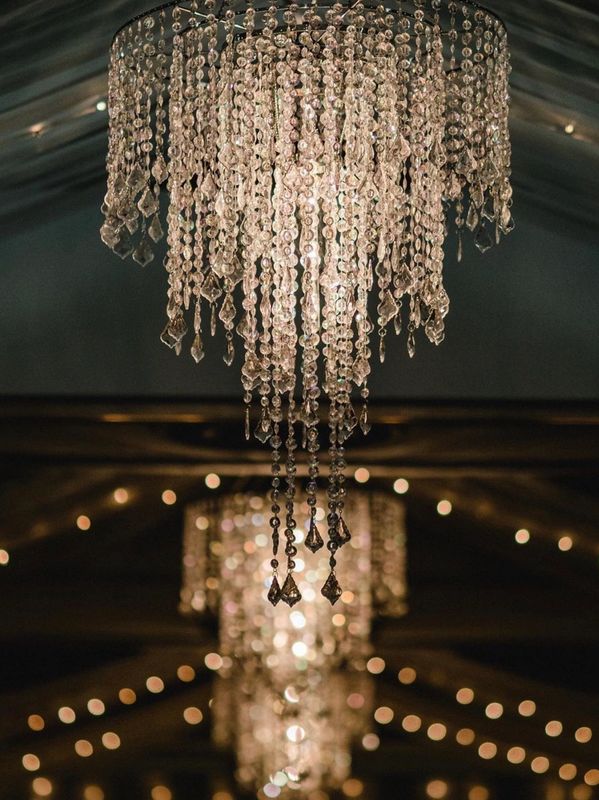 Three tier chandeliers with string lights and drapery in between.