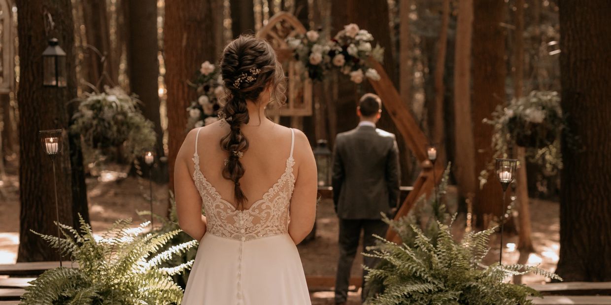 Gorgeous first look in an outdoor forest chapel with mature trees, ferns, candles and wooden benches