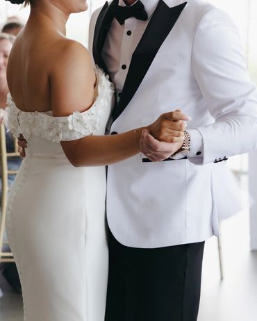 Couple dancing. Her in a white dress, him in a white jacket with black lapels and black pants.