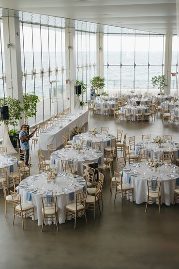 Waterfront venue with floor to ceiling windows that is set up and ready for a wedding reception.