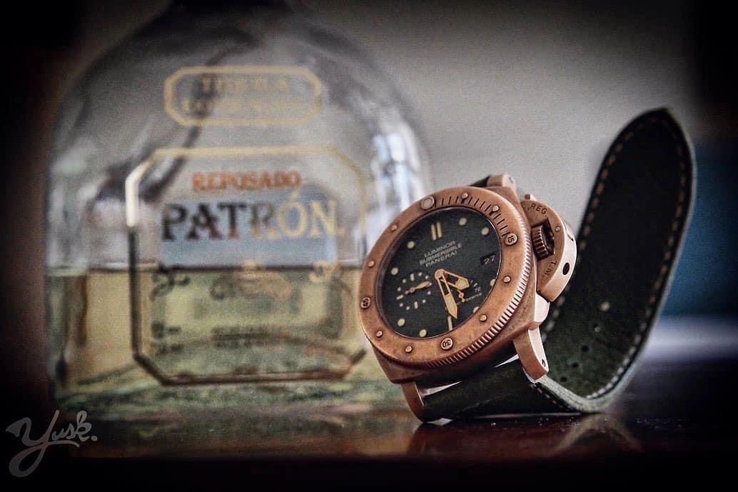 Close-up of a luxury wristwatch with a Patron tequila bottle in the background.
