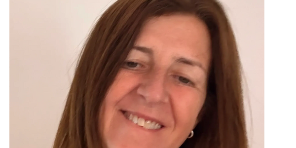 A woman with brown hair smiling gently against a plain background.
