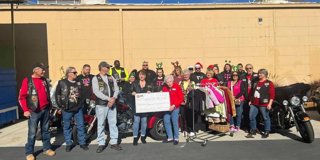 Group photo of diverse people with motorcycles and a big check.