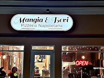 Exterior of Mangia E Bevi pizzeria at night with people dining outside.
