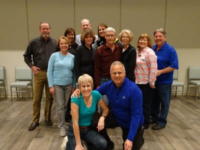 Group of eleven adults posing indoors, smiling and casually dressed.