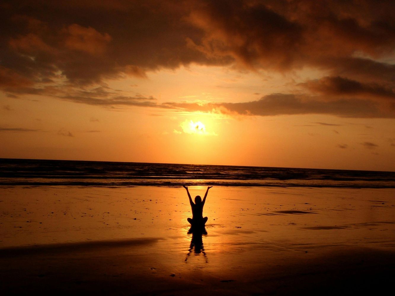 Person silhouetted against a golden sunset on the beach.